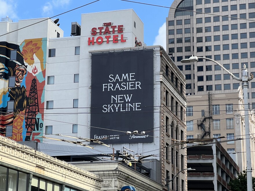 A sign on the wall of a hotel reads 'Same Frasier. New skyline.' in white letters in Florentine Regular font, with a solid black background.