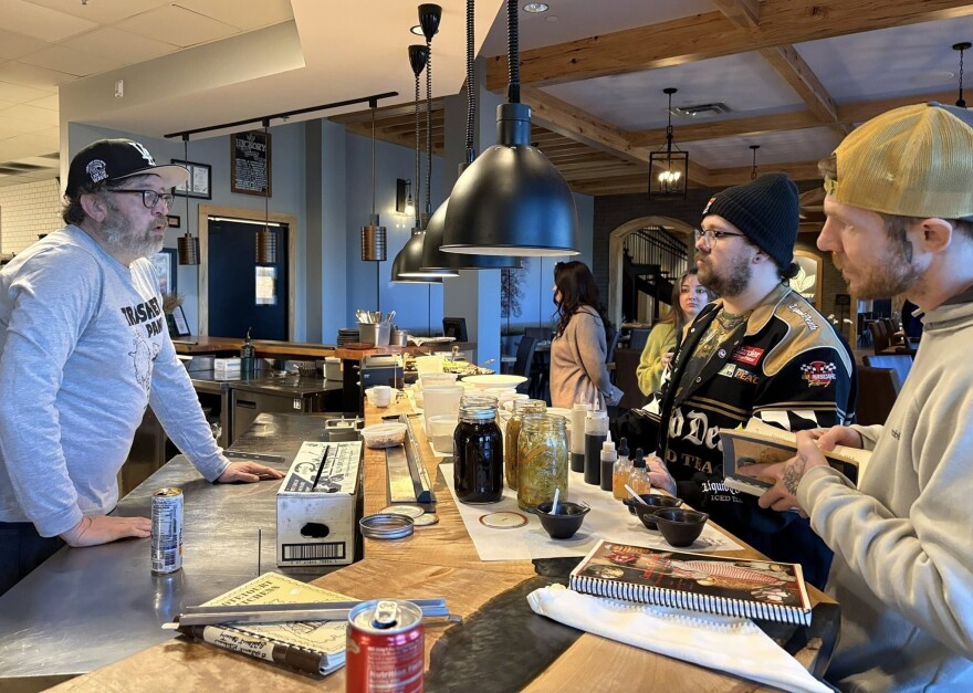 Chef Travis Milton (left speaks to chefs Stephen Doyle (black jacket) and Justin Bailey, wearing a gold cap, about the foods he prepares at a kitchen in Bristol.