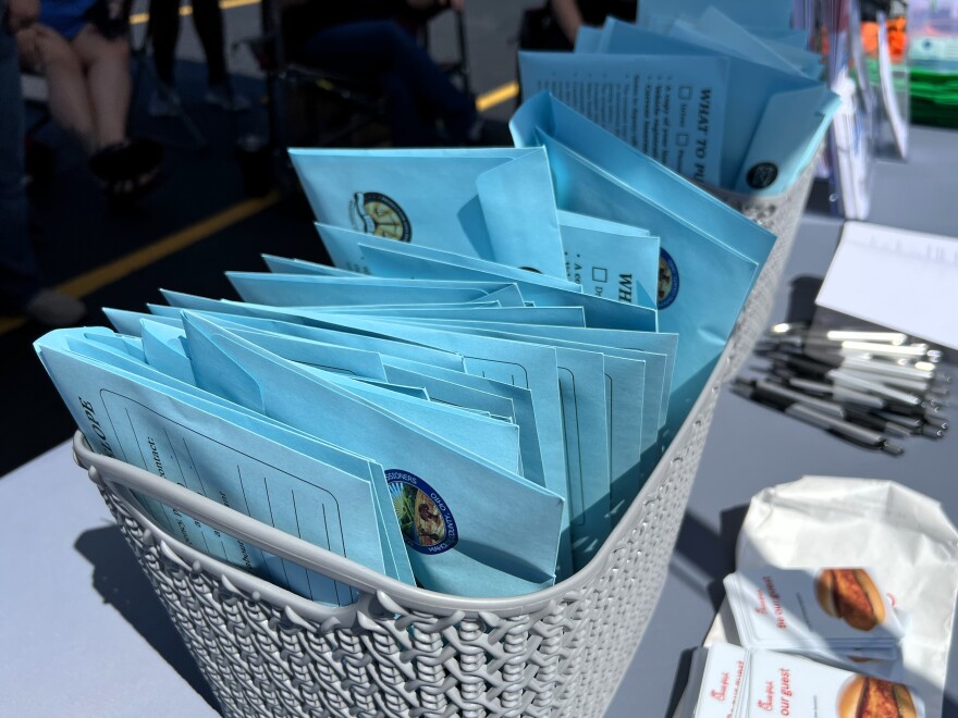 A box filled with blue envelopes sits on a gray table beside piles of pens and other papers.