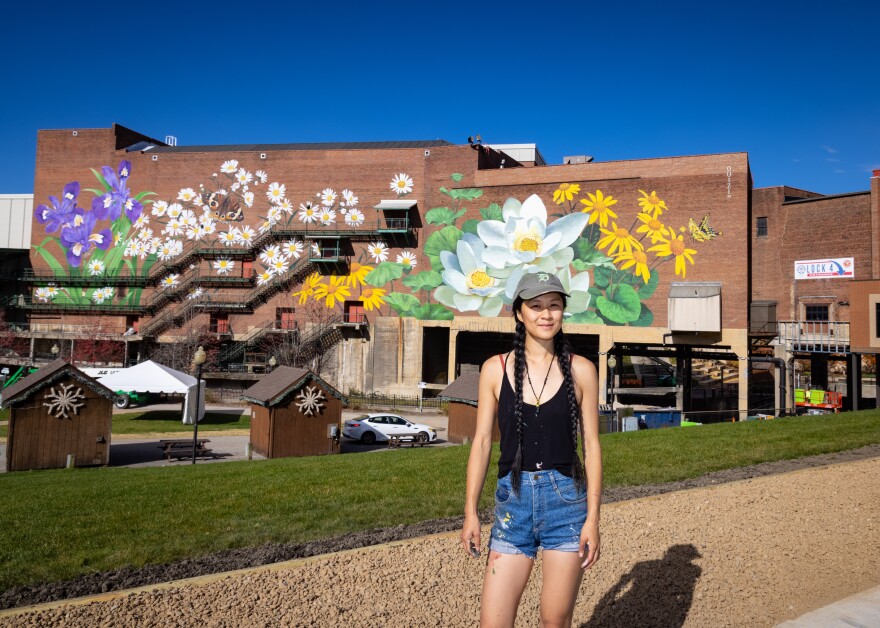 Ouizi, the creator of the mural on the wall behind her, poses in front of her completed work