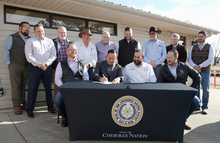 Four men sit at a table bearing the Cherokee Nation seal. Nine men stand behind them. Principal Chief Chuck Hoskin Jr. signs a piece of paper as everyone looks on, smiling.

Front row (from left):Tribal Councilor Daryl Legg, Principal Chief Chuck Hoskin Jr., Roland Town Manager Monty Lenington and Deputy Chief Bryan Warner. 

Back row: Roland Chamber of Commerce Vice President Dave Richards, Roland Chamber of Commerce President Dale Phelps, Roland Town Attorney Jeff Edwards, Roland Vice Mayor Bill Lee, Roland Mayor Randy Hall, Roland City Councilor Blake Rainwater and Roland City Councilor Roger Johnson.