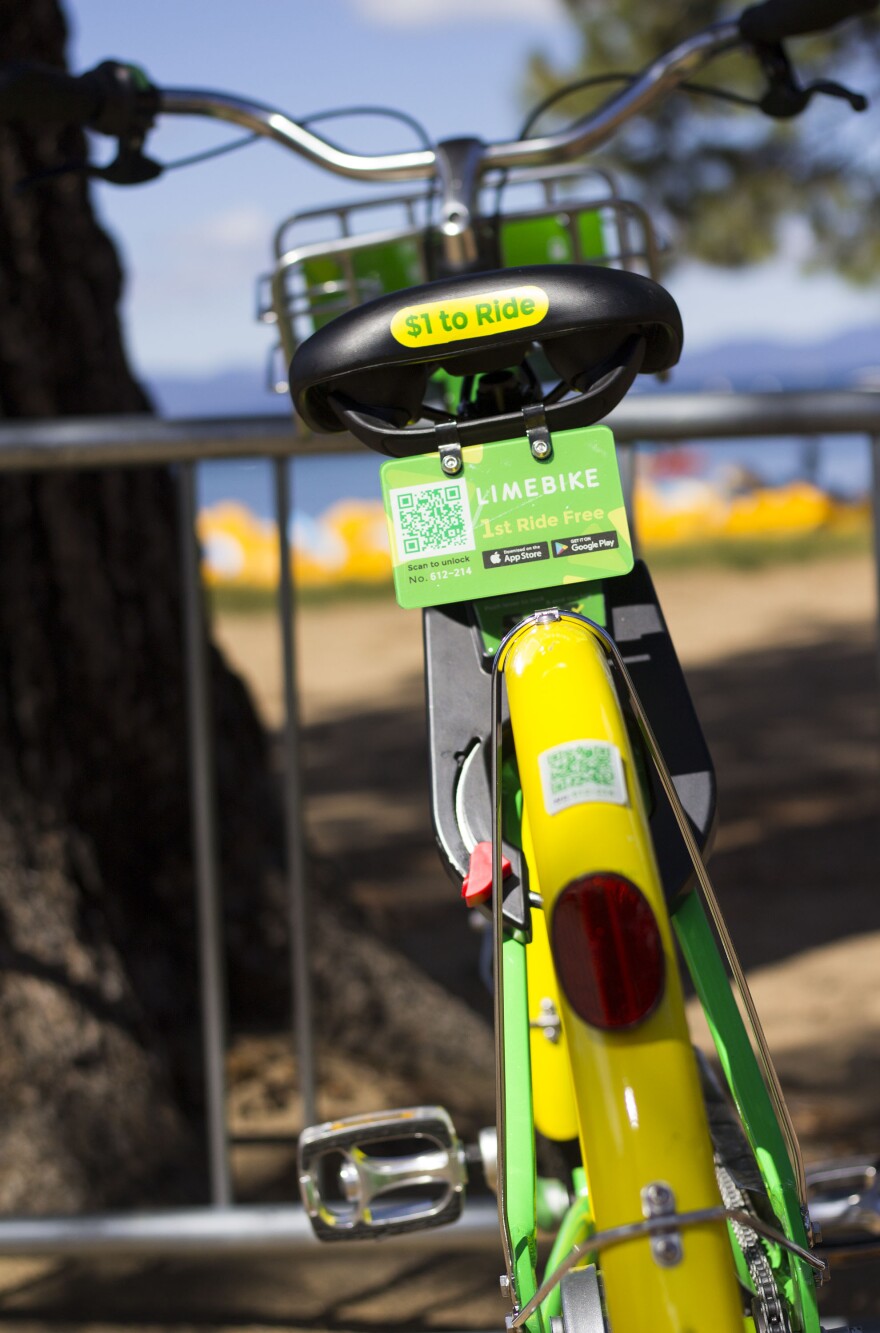 The back of a yellow and green Lime Bike with a small sign on the back saying "1st ride free" and a scannable code.