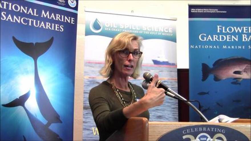 Laura Engleby speaks at a podium during a marine science event, with banners for the National Marine Sanctuaries and the Flower Garden Banks National Marine Sanctuary behind her.