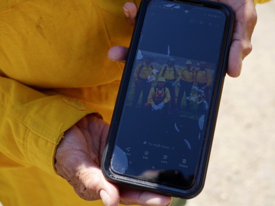 A person holds a phone up to the camera with a photograph of a group of four people wearing firefighting gear.