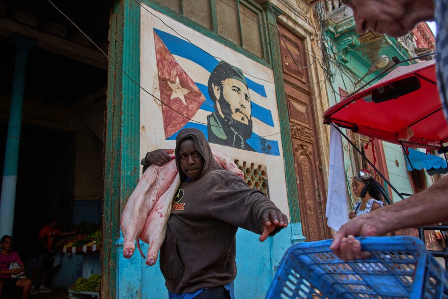 A man carries a pig at the entrance of a market, decorated with a mural of Fidel Castro, in Havana, Cuba, Wednesday, Aug. 12, 2026.