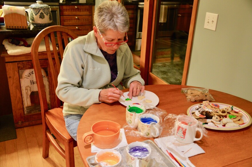 Mary Thode decorates cookies at a table. Mugs of different colored frosting are on the table.