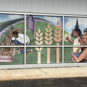 A mural on the outside of the Feeding America Eastern Wisconsin building in Milwaukee depicts a scene of a man tending to crops at the nearby Alice's Garden, and a woman carrying a child who's holding an apple