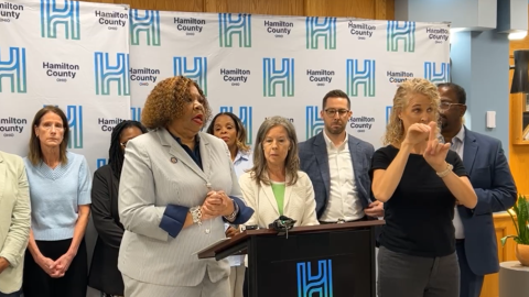 two women stand at a podium with people behind them