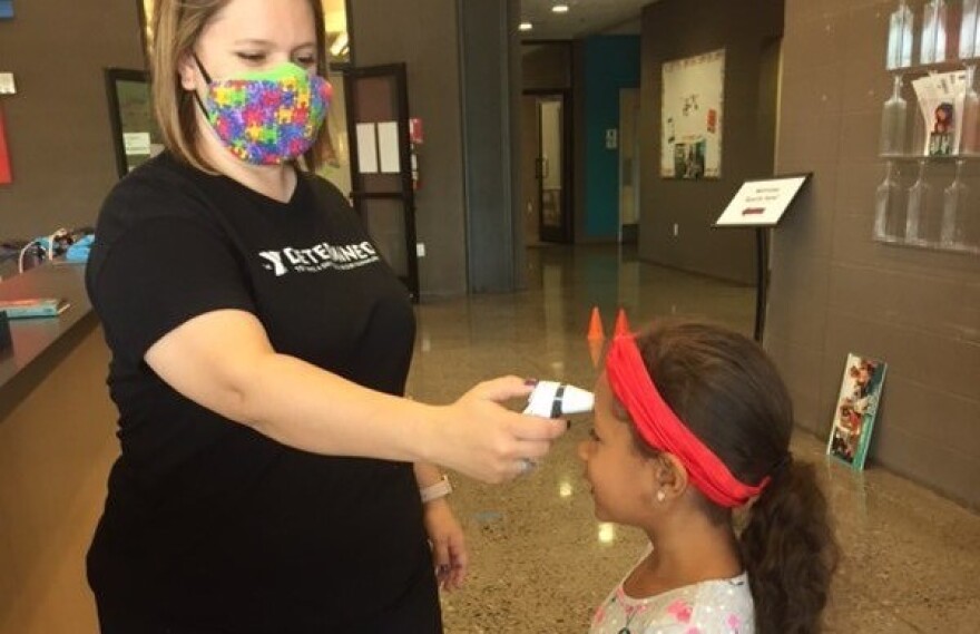 A Valley of the Sun YMCA staff member takes the temperature of a child before she enters child care.