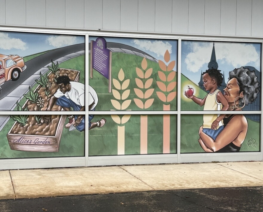 A mural on the outside of the Feeding America Eastern Wisconsin building in Milwaukee depicts a scene of a man tending to crops at the nearby Alice's Garden, and a woman carrying a child who's holding an apple
