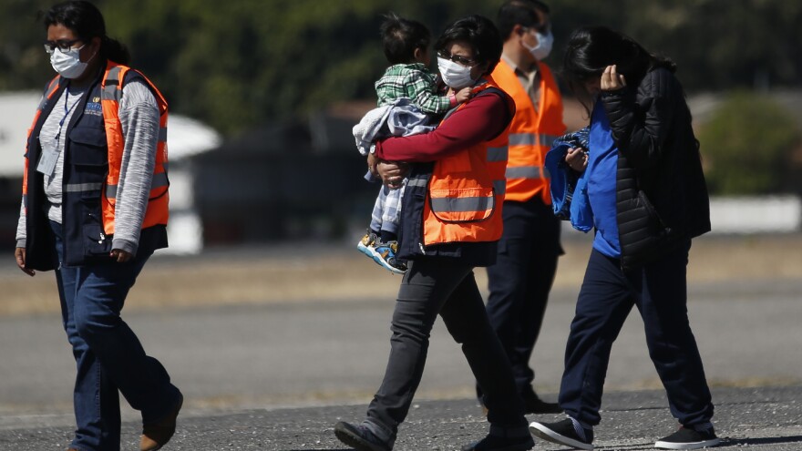 An immigration worker in an orange jacket carries a young Guatemalan deported from the U.S., followed by another deportee, at La Aurora International Airport in Guatemala City on March 12.