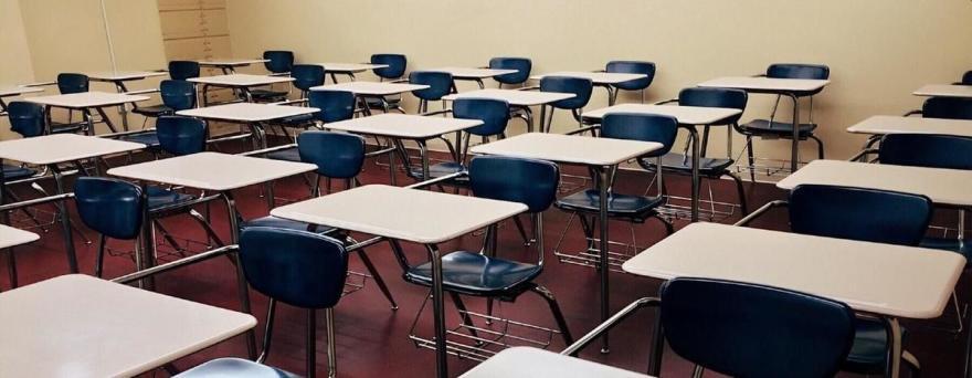 A classroom full of empty white metal desks with blue chairs