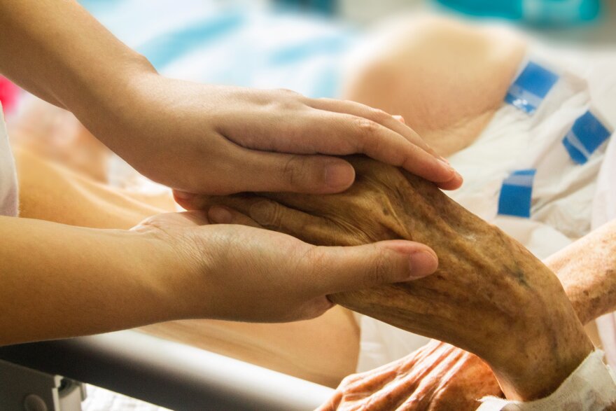A person holding the hand of an elderly person.