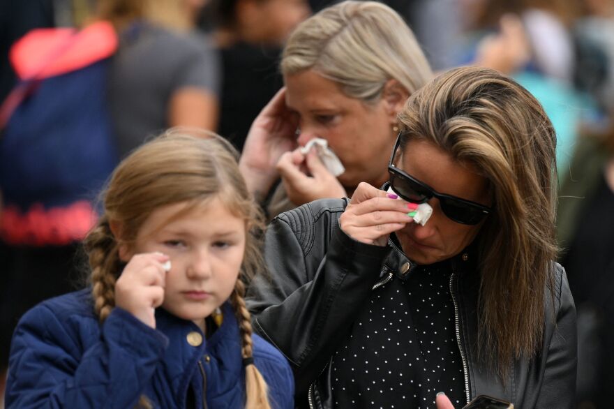 People react after placing flowers and tributes at Buckingham Palace on Friday, a day after Queen Elizabeth II died at the age of 96.