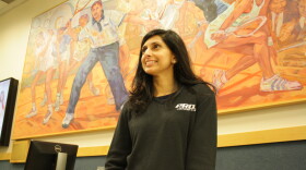 Shabana Khan stands in front of a painting at Pro Sports, Bellevue, that depicts members of her family playing squash. (Shabana is the one in blue, while her brother Azam is in the center of the painting at her left).