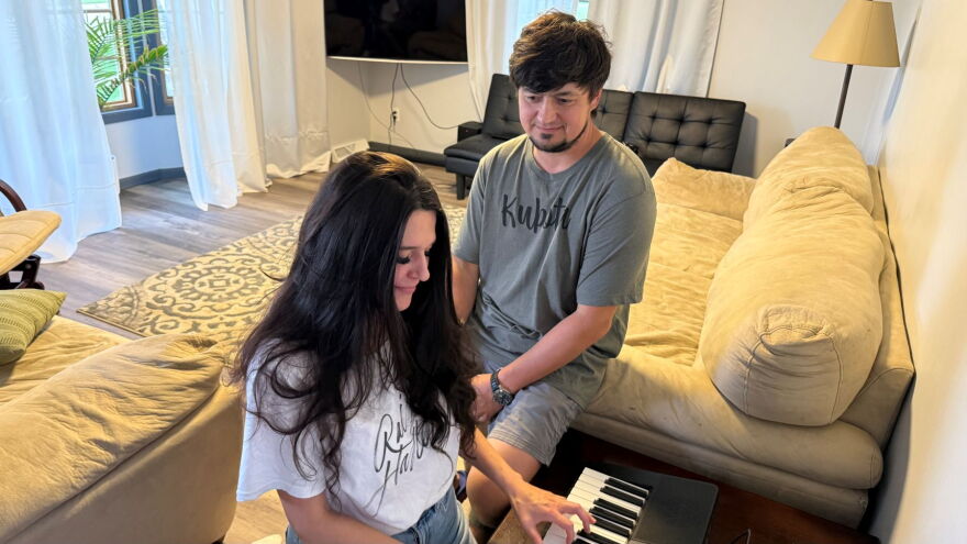 A woman is playing piano with a man looking on.