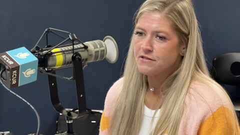A woman sits inside a radio studio and is talking at a microphone.