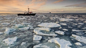 A fishing boat travels through sea ice at sunset