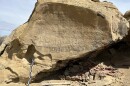 A measuring stick leans against a big boulder outside, which has Indigenous inscriptions on one of its sides.