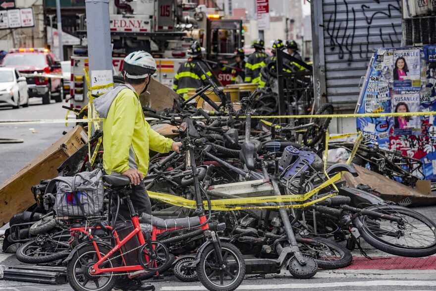 A biker stops to look at a pile of e-bikes in the aftermath of a fire in Chinatown, which authorities say started at an e-bike shop and spread to upper-floor apartments, Tuesday June 20, 2023, in New York. Federal officials are looking into cracking down on defective lithium-ion batteries that power hoverboards, scooters and motorized bicycles because of a rash of deadly fires caused by exploding batteries. 