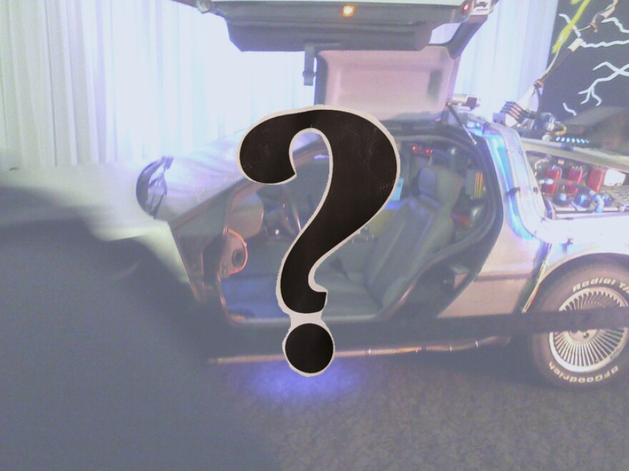 A question mark in the foreground in front of a Delorian with the side door open