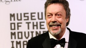 A man in a tuxedo smiles into the camera.