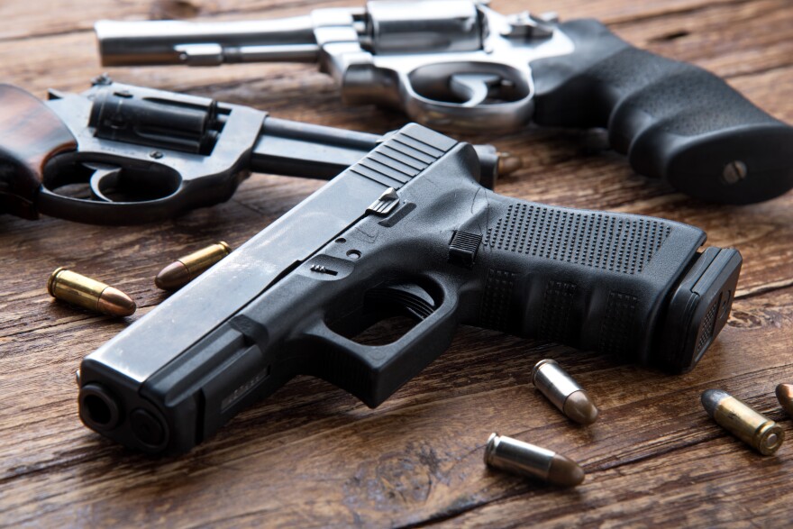 Guns with bullet casings sit on a wooden table. 