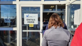 A line of people seen from the back heads through an open door. On a closed glass door next to the line, a sign reads "Franklin County Board of Elections, Enter Here." 