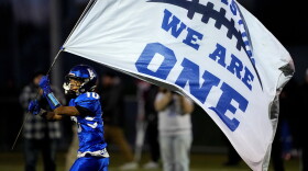 Lewiston High School running back Jayden Sands carries a flag onto the field prior to a football game against Edward Little High School, Wednesday, Nov. 1, 2023, in Lewiston, Maine. Locals seek a return to normalcy after a mass shooting on Oct. 25. (AP Photo/Matt York)