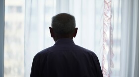 Silhouette of retired man looking through window with transparent curtain