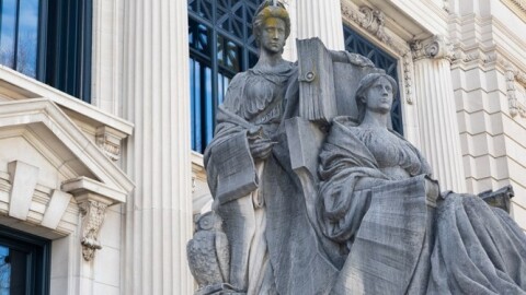 A neoclassical building facade with columns and a large statue of two figures, reminiscent of the Illinois Supreme Court's presence. One figure stands, holding a book, while the other is seated. An owl statue sits at their feet, evoking the wisdom needed for 2023 law and constitutional challenges.