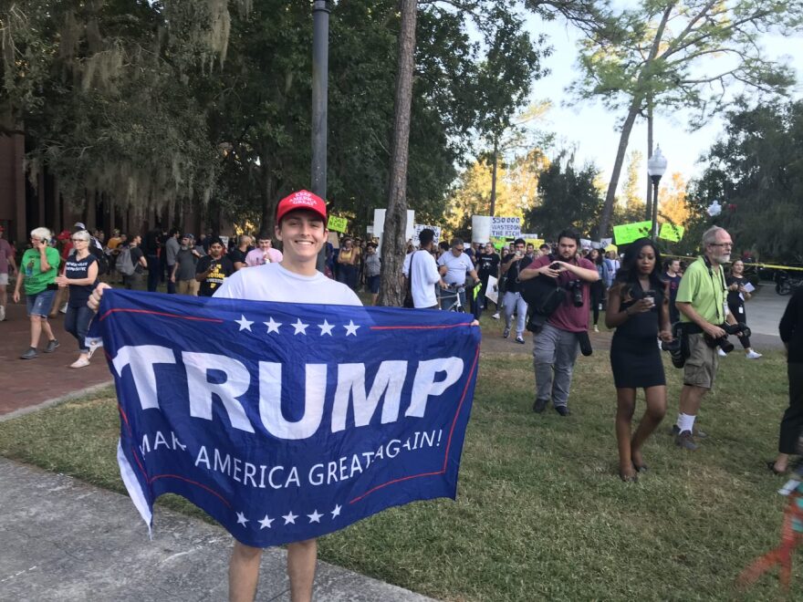 Santa Fe College student Michael Wyatt, 19, shows his support for the Trump administration amid the protest outside the event. (Molly Chepenik/WUFT)