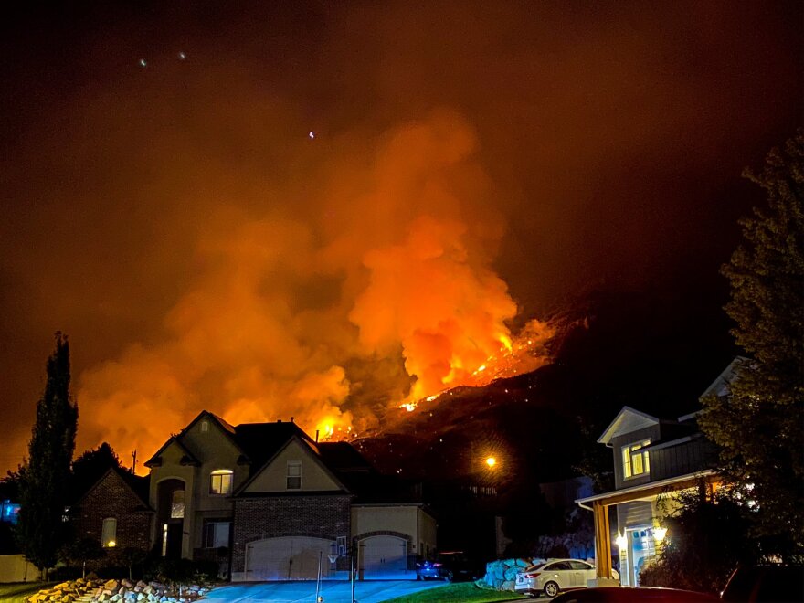 Photo of flames and smoke burning on a hill behind houses.