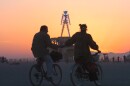 A couple holds hands while cycling near The Man, a stick figured symbol of the Burning Man art festival, during a morning sunrise Saturday, Sept. 3, 2006, at the 20-year-old art festival in Nevada's Black Rock Desert. (AP Photo/Ron Lewis)