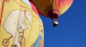 A pilot in an orange-and-red hot air balloon soars above a circus-themed one during the Snowmass Balloon Festival.