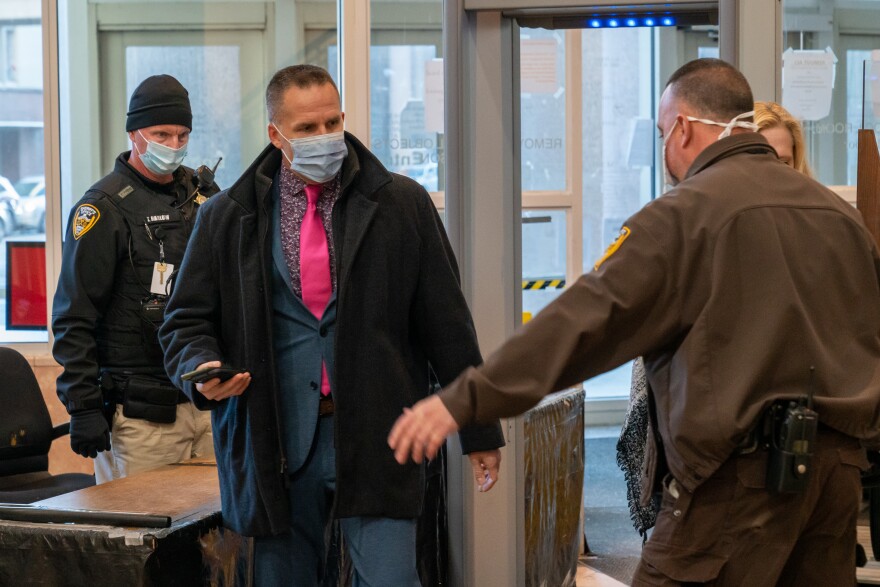 Man wearing surgical mask, dark coat and pink tie goes through security screening