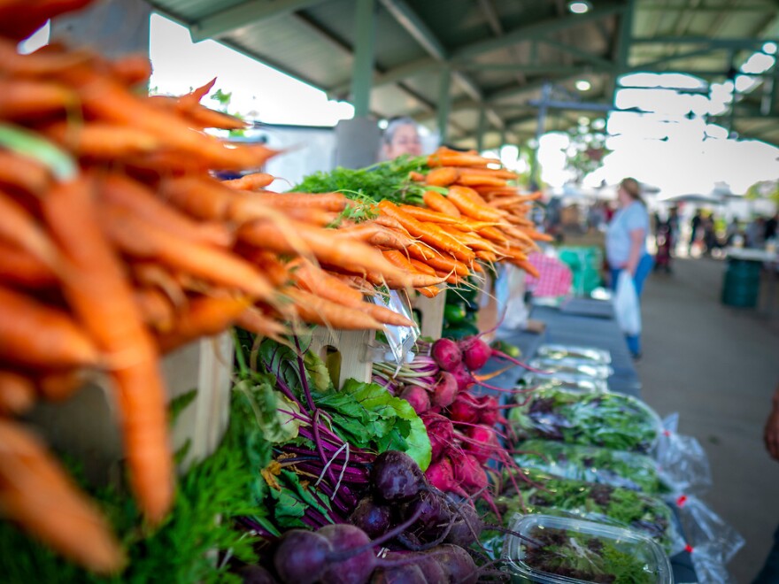 Passersby look at carrots, radishes and beets at a farmers market in Edmond.
