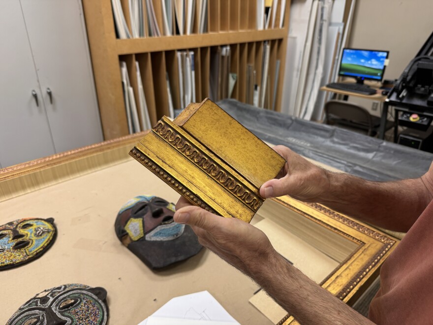 Hands hold two pieces of art frame above table with masks
