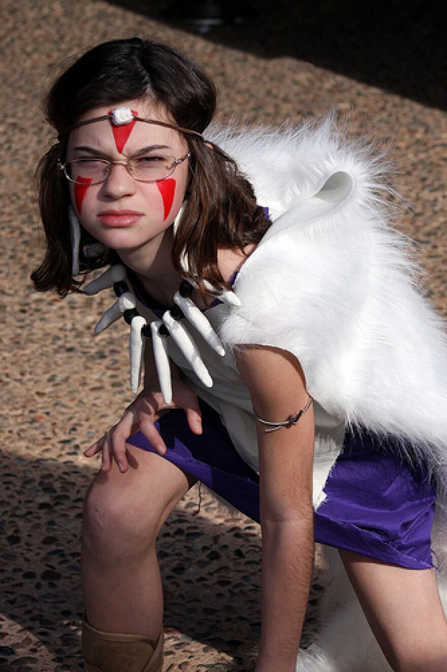 Complete with facepaint, a furry cape and a necklace seemingly made of dinosaur teeth, a young girl with glasses strikes a fierce Princess Mononoke pose.