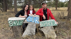Three people lean against three pieces of wood, with the words "Save Our School."