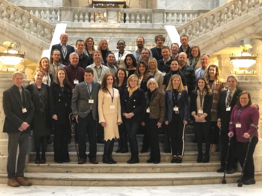 Two dozen people stand on a large marble staircase at the Utah Capitol