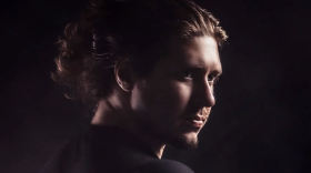 A man with a goatee and hair in a bun is staring off into the distance