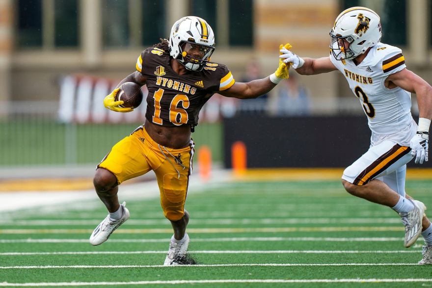 Two men in Wyoming Cowboys football gear run toward each other.