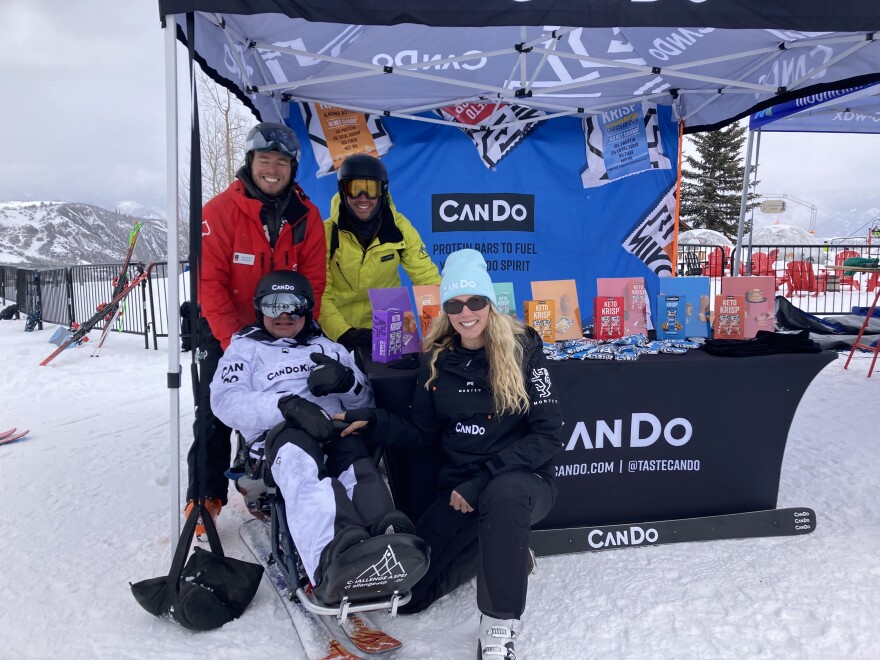 Adam Breman smiles in front of the CanDo tent in his sit ski surrounded by his instructors and employees.