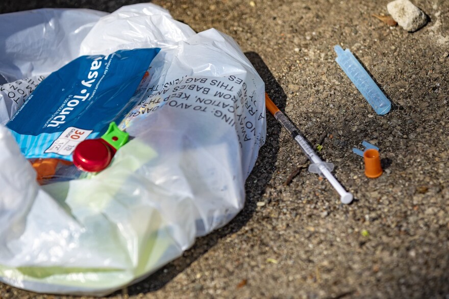 A syringe filled with what is believed to be fentanyl lies on the ground with a bag of other various drug user paraphernalia behind the Universal Missionary Church in Brockton. 