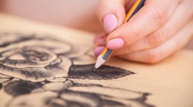 Closeup of woman's hands with a pencil drawing beautiful bunch of roses at the desk