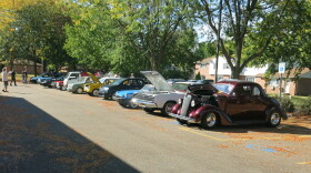 About 10 brightly colored cars and a couple of people milling around them. 