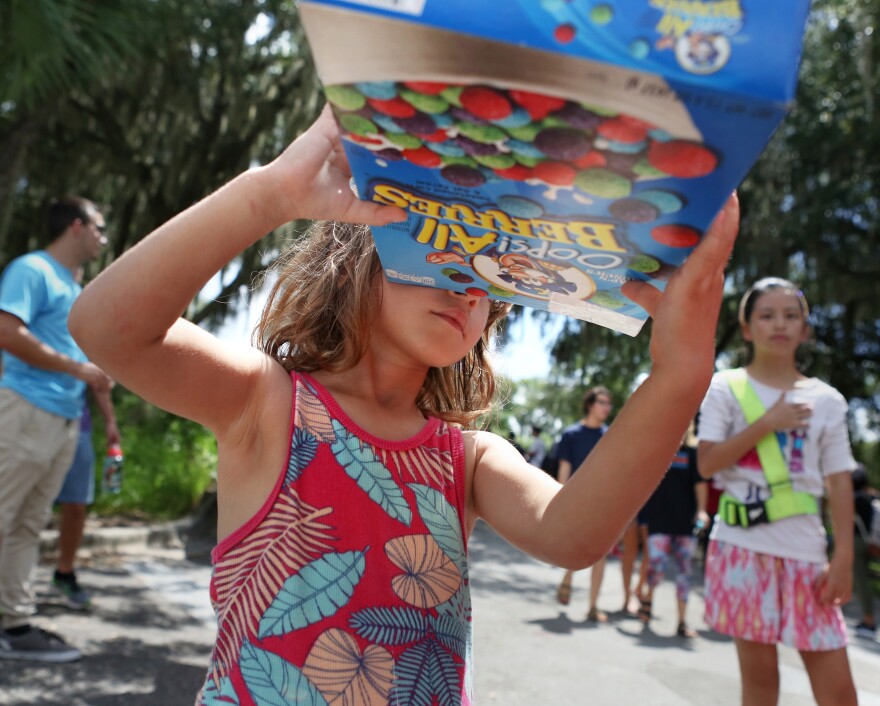 Sarah Carniello, 4, looks at the sun through a Cap’n Crunch cereal box turned pinhole projector during the solar eclipse on Monday. The watch party outside of the Campus Teaching Observatory hosted upwards of 500 people who viewed the phenomena through protected telescopes. (Emma Green/WUFT News)