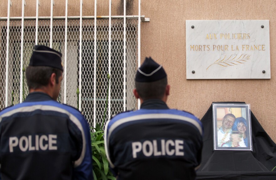 Police officers stand in front of a photo showing a French policeman and his partner, who were killed on June 13 by a man claiming allegiance to the Islamic State group.