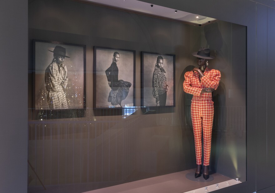 Chris Seydou's orange checkered suit and wide brimmed hat is ready to strut at the "Africa Fashion" show. The three photos of Seydou's clothes on the wall were made by Sierra Leone-born, London-based stylist IB Kamara, now editor-in-chief of the magazine <em>Dazed.</em>